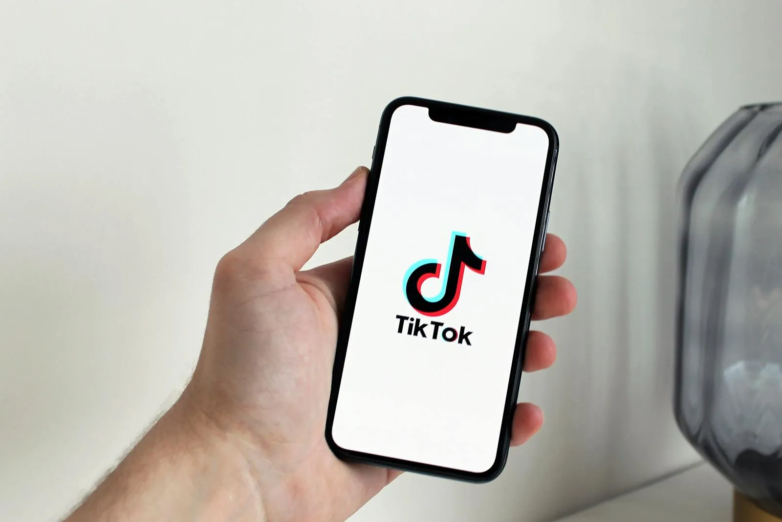 Close-up of a hand holding a smartphone displaying the TikTok app logo.