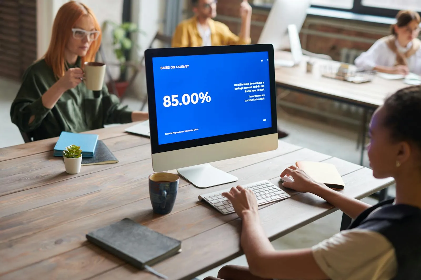 Women collaborating in a modern office space with computers and coffee, emphasizing teamwork.